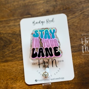 May include: A sparkly pink, blue and black badge reel with the text "Stay in your lane".