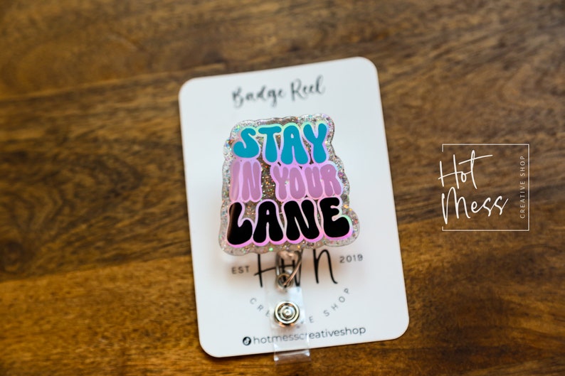 May include: A sparkly pink, blue and black badge reel with the text "Stay in your lane".