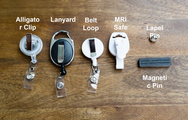 May include: Assortment of badge holders and accessories, including an alligator clip, lanyard, belt loop, MRI-safe clip, lapel pin, and magnetic pin. The image includes text labels for each item, displayed on a wooden surface.