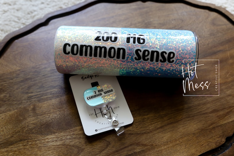 May include: A turquoise and iridescent glitter tumbler with the text "200 mg common sense" and a matching badge reel with the text "2 mg common sense".