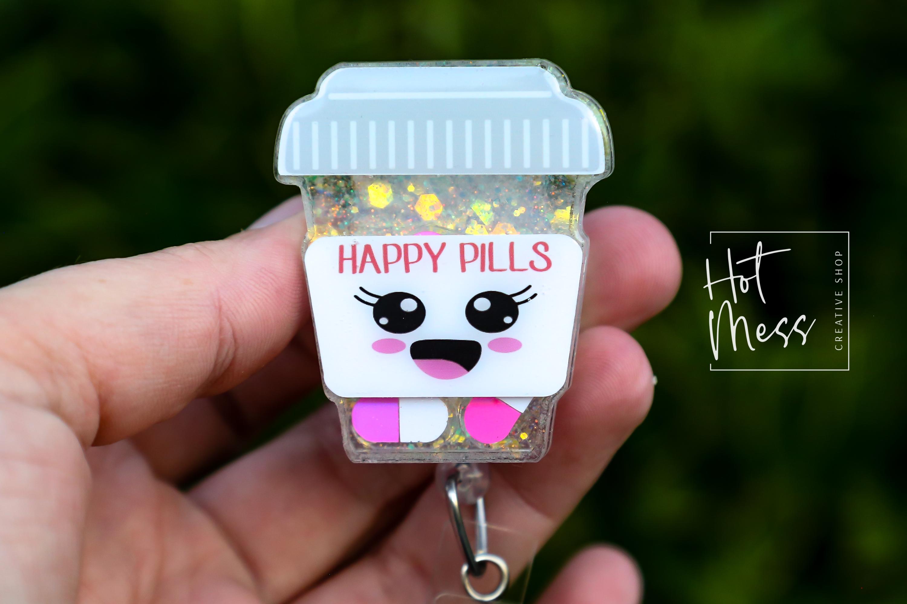 May include: A clear, glitter-filled badge reel shaped like a coffee cup with a light grey lid. The cup features a cartoon face with the words "HAPPY PILLS" and pink and white pills. The reel has a silver clip.
