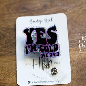 May include: A clear badge reel with a pink and black glitter design that says "YES I'M COLD ME 24:7".
