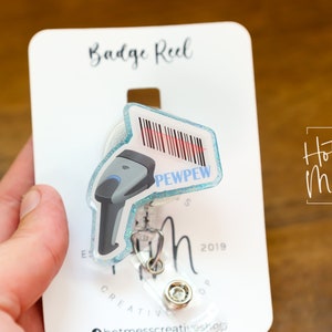 May include: A blue and white badge reel with a barcode and the text "PEWPEW" on it. The reel is attached to a white card with the text "Badge Reel" and "Hot Mess Creative Shop".