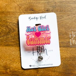 Pode incluir: Carretel de crach&aacute; de glitter rosa com um design "Hot Girl Summer" azul e rosa. O carretel &eacute; preso a um clipe prateado e tem um cart&atilde;o branco com o texto "Hot Mess Creative Shop" e "Badge Reel" impresso nele.
