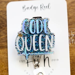 May include: A blue and silver glitter badge reel with the text "CODE QUEEN!" and a small gold crown. The badge reel is attached to a white card with the text "Badge Reel" and "Hot Mess Creative Shop" printed on it.