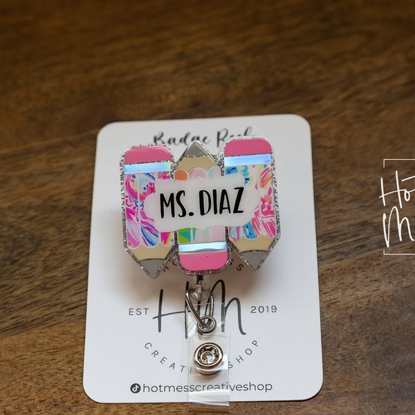 May include: A silver retractable badge holder with a pink, yellow, and blue pencil design. The pencil design has a white cloud with the text "MS. DIAZ" on it. The badge holder is on a white card with the text "Hot Mess Creative Shop" and "Est. 2019".