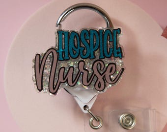 Könnte beinhalten: Ein Ausweis-Rollhalter mit den Worten "HOSPICE Nurse" in türkis und rosa Glitzer. Die Rolle hat einen silbernen Karabinerhaken und einen transparenten Kunststoff-Gürtelclip.