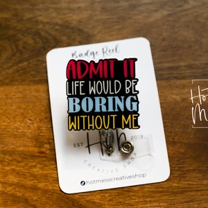 May include: A white card with the text "Badge Reel Admit It Life Would Be Boring Without Me" in colorful letters. The card also has the text "Hot Mess Creative Shop" and a small clear badge reel with a silver clip.