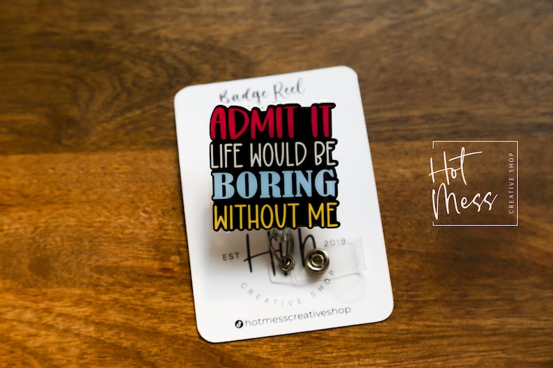 May include: A white card with the text "Badge Reel Admit It Life Would Be Boring Without Me" in colorful letters. The card also has the text "Hot Mess Creative Shop" and a small clear badge reel with a silver clip.