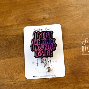 May include: A black badge reel with a pink and purple gradient design. The text on the reel reads "I kept the inside thoughts inside". The reel is attached to a silver retractable badge holder.