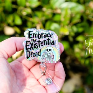 May include: A pink glitter badge holder with a skeleton holding a coffee cup and the text "Embrace the Existential Dread".