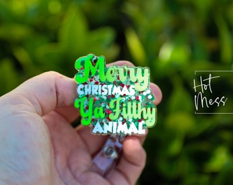 Könnte beinhalten: Ein glitzernder Badgehalter in Grün, Rot und Weiß mit dem Text "Merry Christmas Ya Filthy Animal".