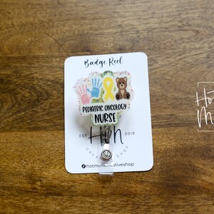 Peut inclure: Porte-badge blanc avec un fond paillet&eacute; et un insert en plastique transparent. L'insert pr&eacute;sente un ruban jaune, deux empreintes de mains et un ours en peluche brun. Le texte "Pediatric Oncology Nurse" est imprim&eacute; sur l'insert. Le texte "Hot Mess Creative Shop" est imprim&eacute; au bas du porte-badge.