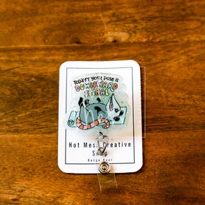 Op de afbeelding: Een witte badge reel met een cartoon illustratie van een rat in een yoga pose op een blauwe mat. De tekst "Today's yoga pose is downward spiral" staat boven de illustratie. De badge reel heeft de tekst "Hot Mess Creative Shop" en een doorzichtige plastic hoes.