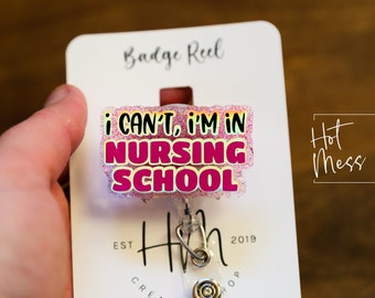 May include: Pink glitter badge reel with the text "I CAN'T, I'M IN NURSING SCHOOL". The badge reel is attached to a white card with the text "Badge Reel" and "Hot Mess Creative Shop".