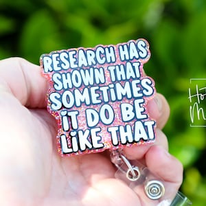 Op de afbeelding: Roze glitter badgehouder met een witte tekstoverlay die "Research has shown that sometimes it do be like that" luidt.