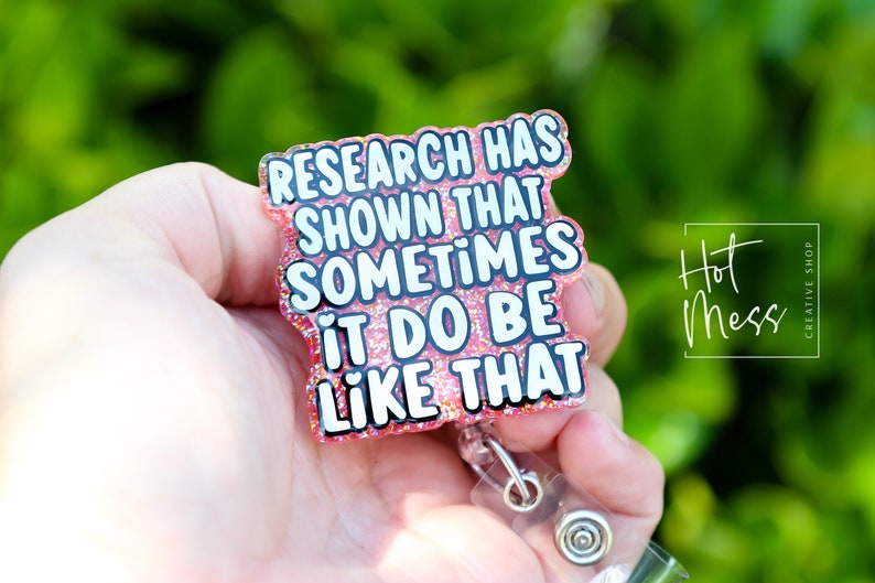 Op de afbeelding: Roze glitter badgehouder met een witte tekstoverlay die "Research has shown that sometimes it do be like that" luidt.