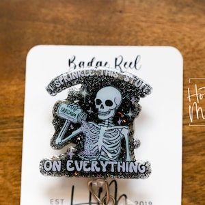 Könnte beinhalten: Ein schwarzer und weißer Glitzer-Badge-Rollenhalter mit einem Skelett, das eine Flasche mit der Aufschrift "viel Sarkasmus" hält. Der Text auf dem Badge-Rollenhalter lautet "Ich streue dieses Zeug überall hin".