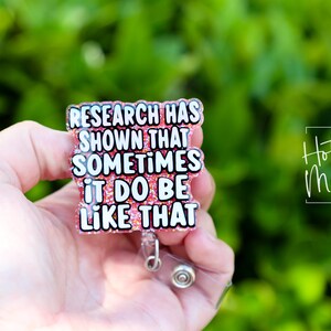 Op de afbeelding: Een roze glitter badgehouder met een witte tekstoverlay die "Research has shown that sometimes it do be like that" luidt.