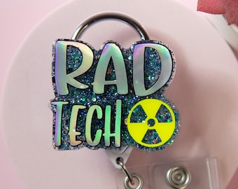 Pode incluir: Um porta-crachá Rad Tech com as palavras "RAD TECH" em letras brilhantes verde-azulado. O porta-crachá tem um clipe de metal prateado e uma alça de plástico transparente. Um símbolo de radiação amarelo também está presente.