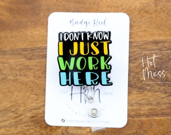 以下が含まれることがあります： カラフルな文字で「I don't know I just work here」と書かれた黒いバッジリール。バッジリールは、「Badge Reel」と「Hot Mess Creative Shop」の文字が印刷された白いカードの上に置かれています。