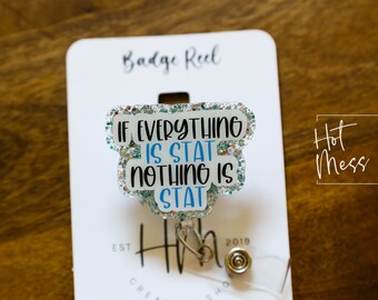 May include: A white badge reel with a silver glitter background and blue text that reads "If everything is stat nothing is stat". The badge reel is attached to a silver retractable badge holder. The badge reel is on a white card with the text "Badge Reel" and "Hot Mess Creative Shop" printed on it.