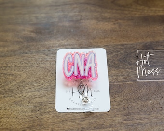 May include: Pink and white glitter CNA badge reel with a silver retractable badge holder. The badge reel has the text "Hot Mess Creative Shop" and "Est 2019" on it.