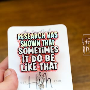 Op de afbeelding: Roze glitter badgehouder met een witte tekstoverlay die "Research has shown that sometimes it do be like that" luidt.