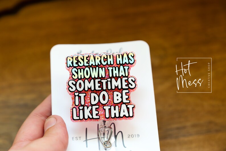 Op de afbeelding: Roze glitter badgehouder met een witte tekstoverlay die "Research has shown that sometimes it do be like that" luidt.