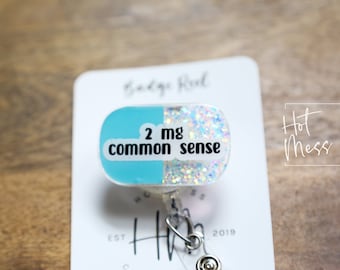 Puede incluir: Un carrete de credencial en forma de píldora azul y blanco con purpurina y el texto "2 mg de sentido común".