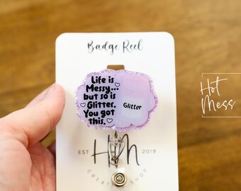 May include: A purple glitter badge reel with the text "Life is Messy... but so is Glitter. You got this." and a small heart after each word. The badge reel is on a white card with the text "Badge Reel" at the top and "Hot Mess" at the bottom.