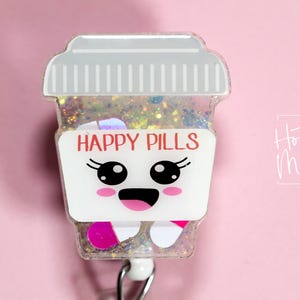 May include: A badge reel with a cartoon pill bottle design. The bottle is white and clear, with the words "HAPPY PILLS" and a smiling face. The background is pink.