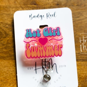 Pode incluir: Carretel de crach&aacute; de glitter rosa com um design "Hot Girl Summer" azul e rosa. O carretel &eacute; preso a um suporte de crach&aacute; retr&aacute;til prateado.