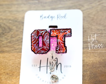 Puede incluir: Un carrete de identificación de brillo rosa y rojo con las letras "OT" en un patrón floral blanco y rojo. El carrete de identificación está unido a un cordón retráctil plateado. El texto "Badge Reel" está impreso en una tarjeta blanca detrás del carrete de identificación. El texto "Hot Mess Creative Shop" está impreso en la tarjeta en la esquina inferior derecha.