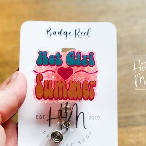 Pode incluir: Um carretel de crach&aacute; de glitter rosa com uma fonte retr&ocirc; turquesa e laranja que diz "Hot Girl Summer" e um cora&ccedil;&atilde;o vermelho. O carretel de crach&aacute; est&aacute; preso a um cart&atilde;o branco com o texto "Badge Reel" e "Hot Mess Creative Shop" impresso nele.