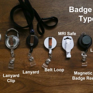 May include: A close-up of eight different types of badge reels, including alligator clip, lanyard clip, lanyard, belt loop, MRI safe, magnetic badge reel, and lapel pin.  The badge reels are displayed on a wooden surface.