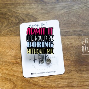 May include: White badge reel with the text "Badge Reel ADMIT IT LIFE WOULD BE BORING WITHOUT ME" in colorful letters. The badge reel has a clear plastic cover with two silver badge clips.