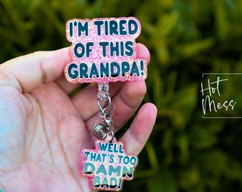 May include: Pink glitter badge reel with the text "I'm tired of this grandpa!" and a smaller pink glitter charm with the text "Well that's too damn bad!"