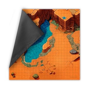 May include: A square, orange-toned gaming mat with a grid pattern, depicting a desert landscape with a river, rock formations, and a structure. The mat has a dark gray backing, partially visible. The design includes shades of blue, brown, and green.