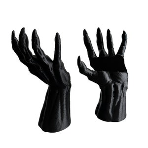Peut inclure: Deux mains noires, détaillées, imprimées en 3D avec de longs doigts, posées avec les paumes vers le haut.