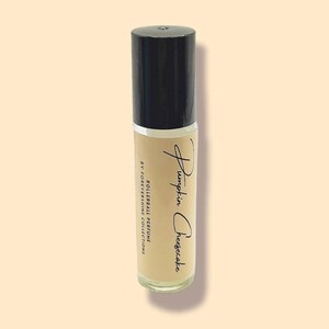 May include: A clear glass rollerball perfume bottle with a black cap. The bottle is labeled "Pumpkin Cheesecake" and "Rollerball Perfume" by "Forevershine Collections".