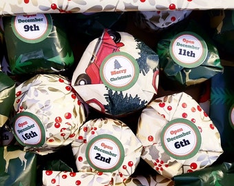 May include: A collection of small, individually wrapped gifts featuring festive holiday patterns in red, green, and cream. Each package has a circular label with text such as Merry Christmas and specific dates to open, including December 2nd, 4th, 6th, 9th, 11th, and 16th.