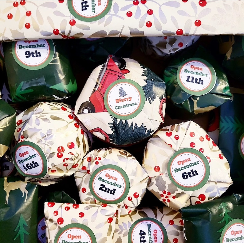 May include: A collection of small gifts wrapped in festive paper featuring red berries, green leaves, and a red truck illustration. Each package has a circular sticker with text such as Merry Christmas or Open December followed by a specific date.
