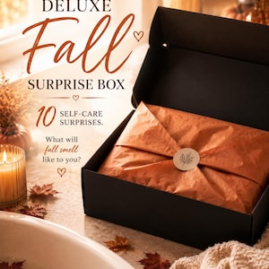 May include: A black cardboard box containing orange tissue paper secured with a circular sticker featuring a leaf illustration. The text reads: DELUXE Fall SURPRISE BOX, 10 SELF-CARE SURPRISES. What will fall smell like to you? The box is open.
