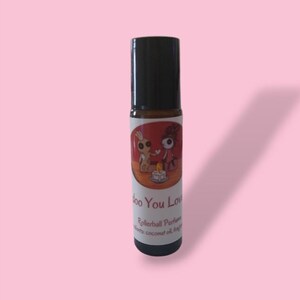 May include: A small glass bottle with a black rollerball top. The label is red with a cartoon illustration of two figures and the text "Do You Love" and "Rollerball Perfume".