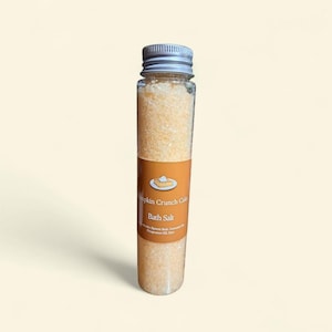 May include: A clear glass tube filled with light orange bath salts. The tube has a silver cap and a label that reads "Pumpkin Crunch Cake Bath Salt" with a graphic of a slice of pie.