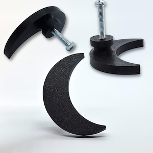 Peut inclure: Tirants de meubles noirs en forme de croissant de lune avec vis attachées. La quincaillerie est faite d'un matériau texturé. Les poignées sont conçues pour être montées sur une armoire ou un tiroir. L'image montre les poignées sous différents angles.