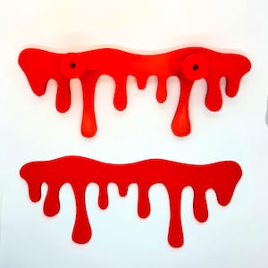 May include: Two red wall hooks and a red decorative piece, all in a dripping paint design, against a white background. The hooks have circular knobs. The design is a bold, modern accent.