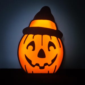 May include: A black and orange Halloween pumpkin with a witch's hat. The pumpkin is lit from inside, creating a warm glow.