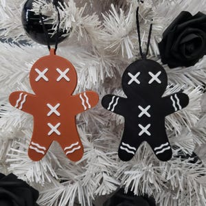 May include: Two gingerbread man ornaments, one brown and one black, with white X's for eyes and mouth. Both have white wavy lines on their arms and legs.